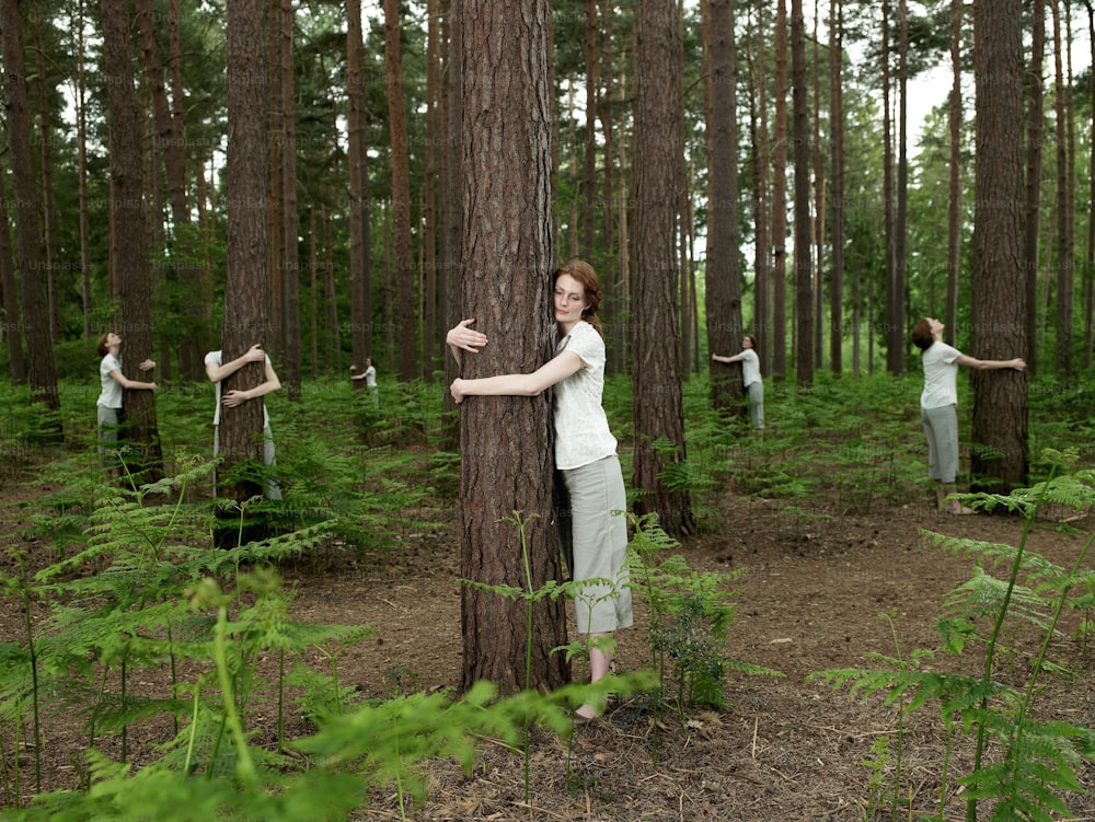 a woman standing next to a tree in a forest