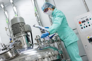 scientist in blue lab uniform stand near big pressure tank , hold tablet , look at camera, turned