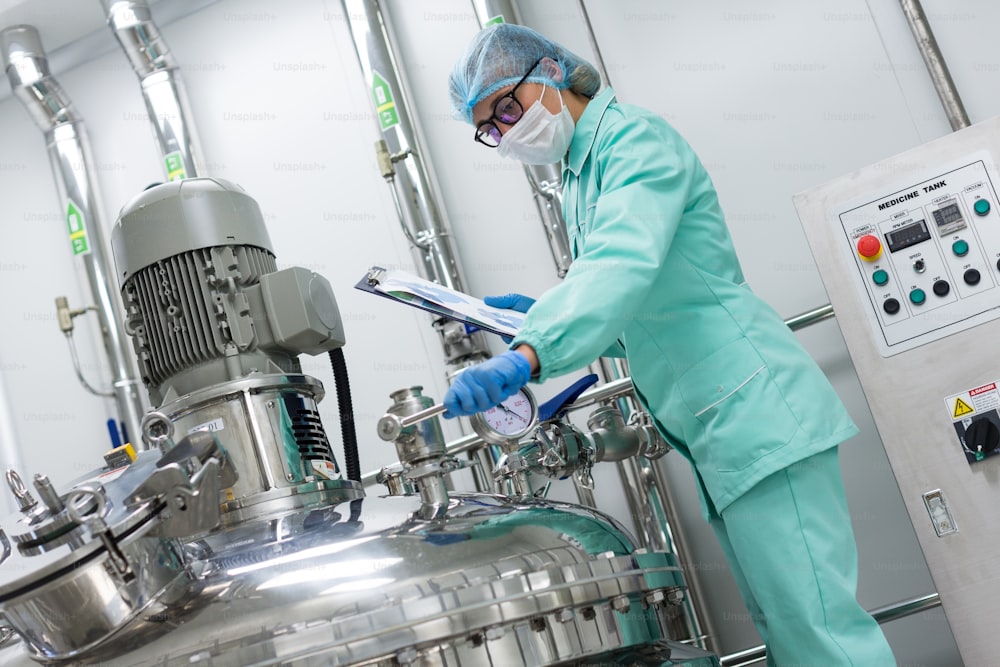 scientist in blue lab uniform stand near big pressure tank , hold tablet , look at camera, turned