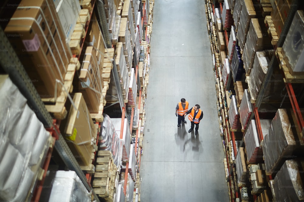 Two men in uniform standing in aisle between large-scale shelves and talking