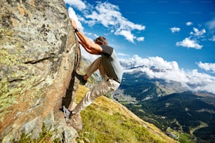 Adult man climbs on a big stone, against a blue sky and valley with Zermatt town