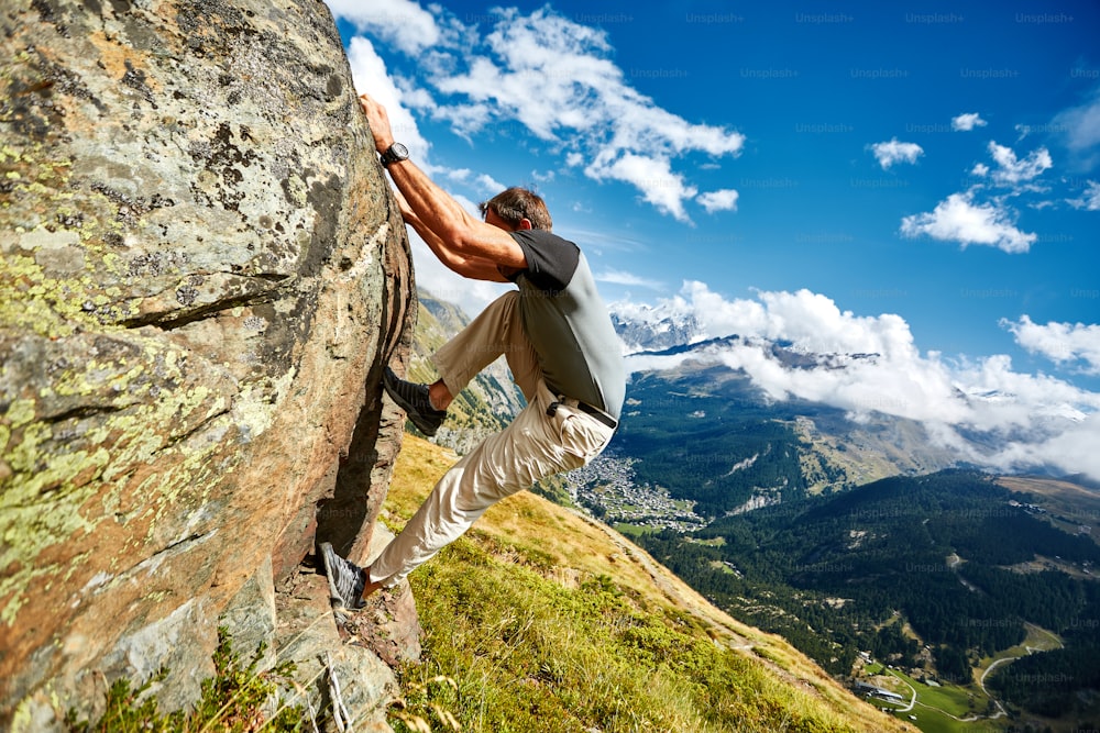 Adult man climbs on a big stone, against a blue sky and valley with Zermatt town