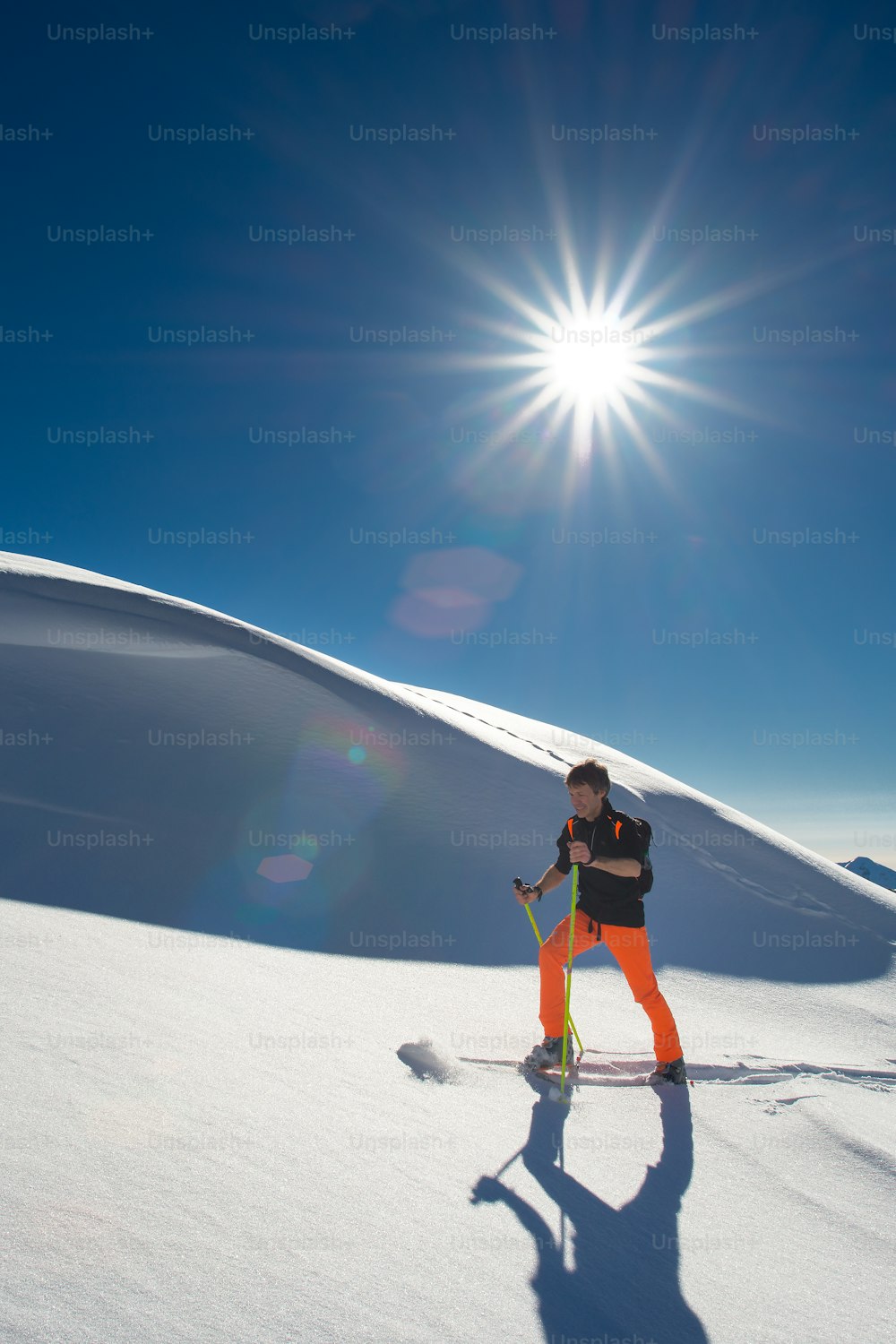 남자 알파인 스키어가 강한 화창한 날에 신선한 눈 속에서 스키와 물개 가죽을 타고 등반합니다.