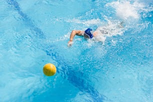 Un hombre nadando en una piscina con una pelota amarilla