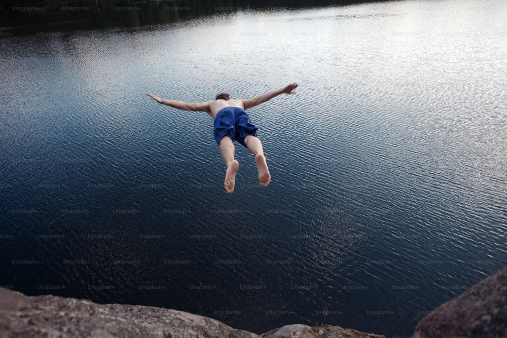 Joven saltando al agua desde el acantilado (hombre en el desenfoque del movimiento)