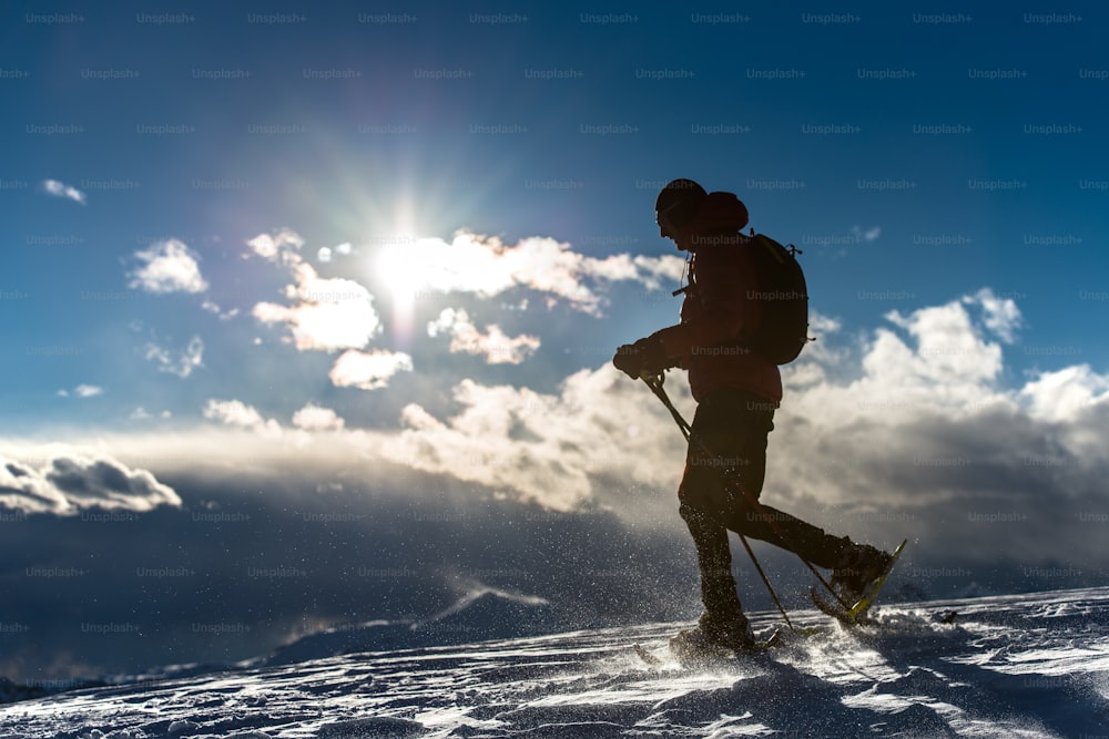Homem andando na neve com raquetes de neve em uma paisagem montanhosa