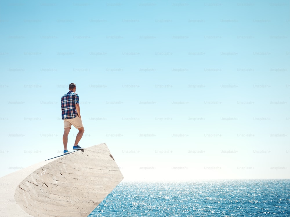 Hombre joven de pie en un pico y mirando el mar