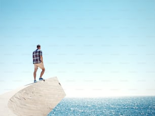 Young man standing on a peak and looking at the sea