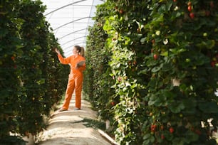 a woman in an orange jumpsuit standing in a greenhouse