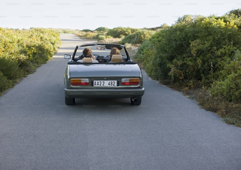 a couple of people in a convertible car on a road