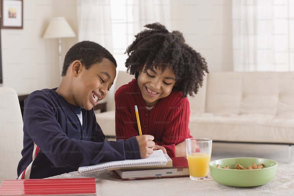 a boy and a girl sitting at a table with a book and a pencil