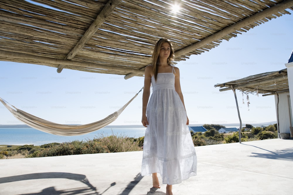 a woman in a white dress is standing under a hammock