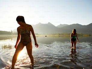 two women in a body of water with mountains in the background