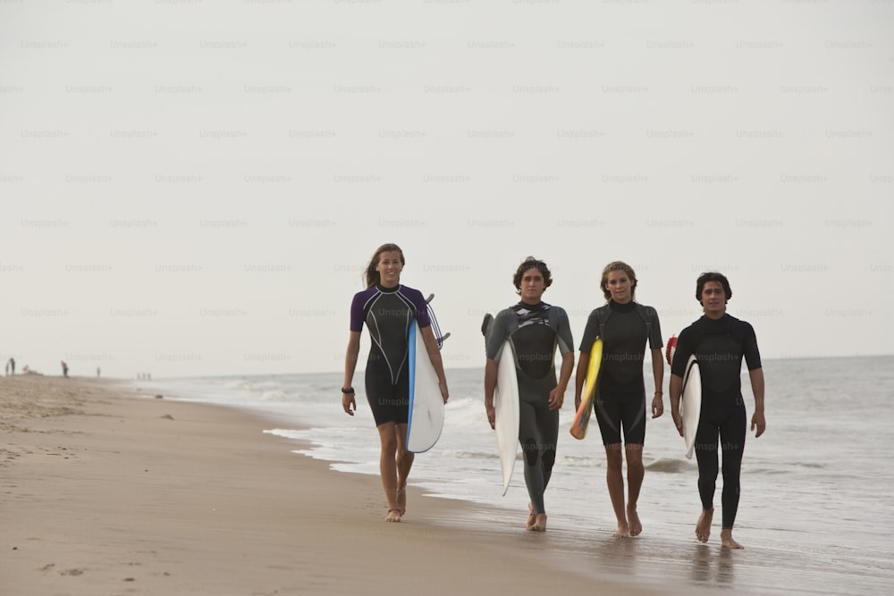 a group of people walking along a beach with surfboards