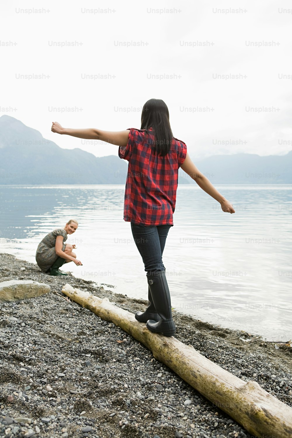 a woman standing on top of a log next to a body of water