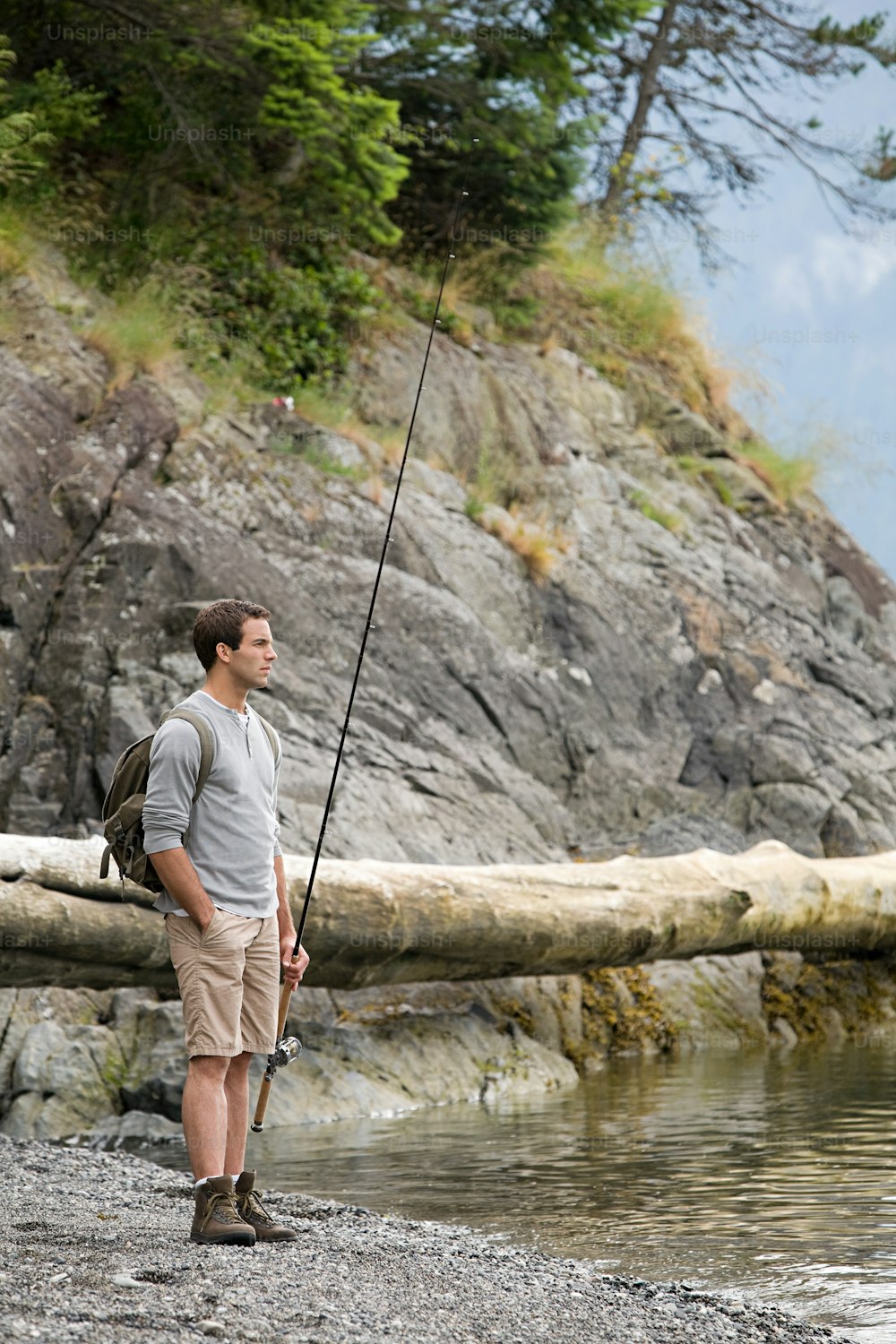 a man standing next to a body of water holding a fishing pole