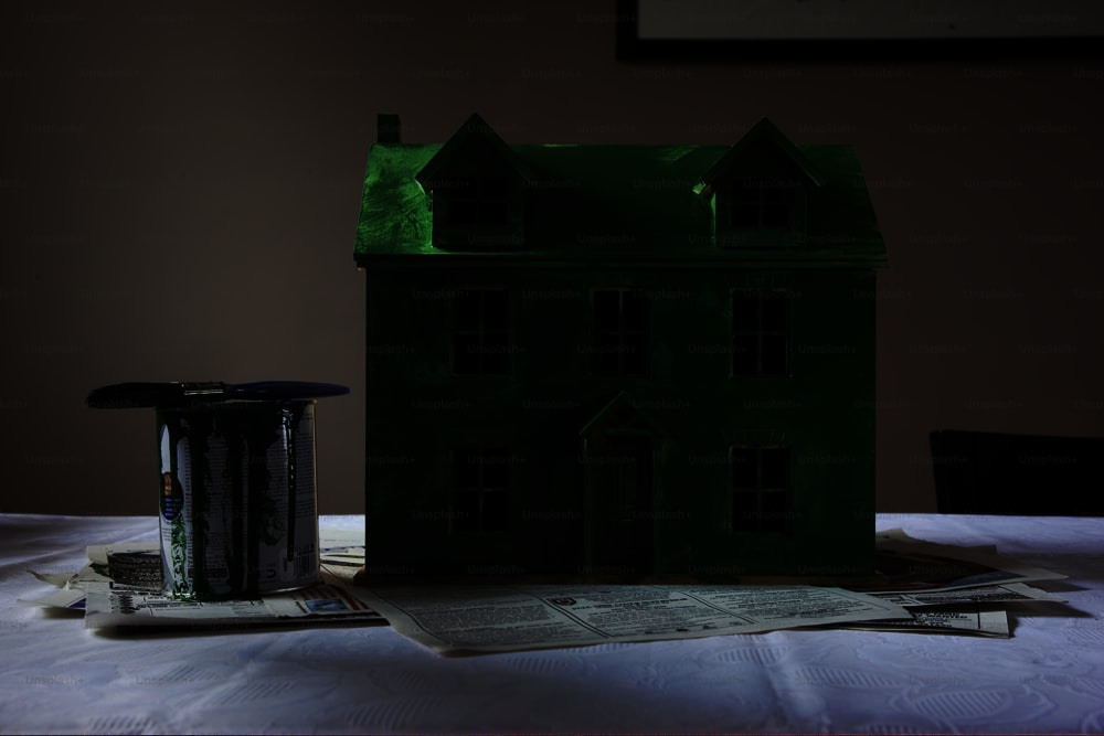 Une maison modèle verte assise sur une table à côté d’un pot de peinture