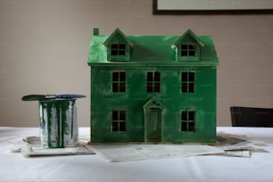 Una casa modello verde seduta sopra un tavolo accanto a una lattina di vernice