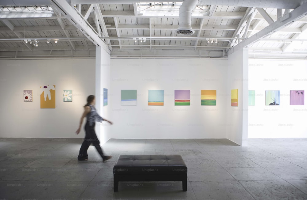 a woman walking through an art gallery with paintings on the wall