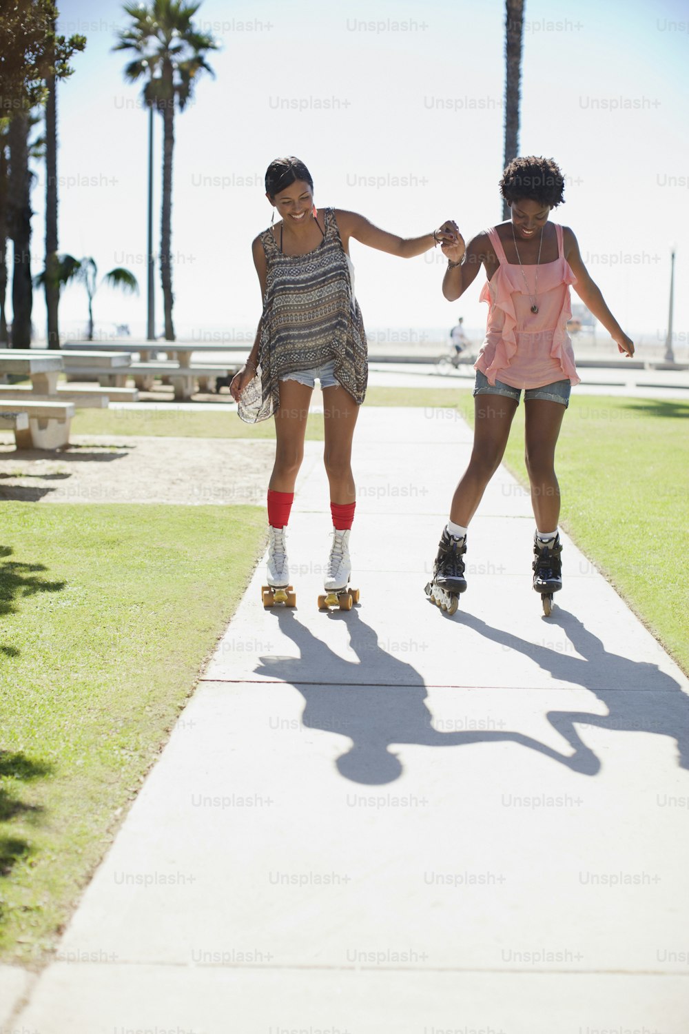 two women rollerblading down a sidewalk near palm trees