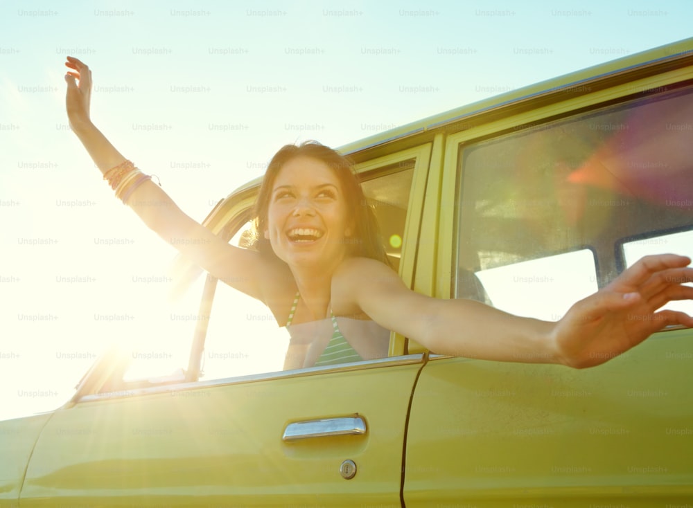 Pretty young woman with her arms outstretched while riding in a car on a roadtrip