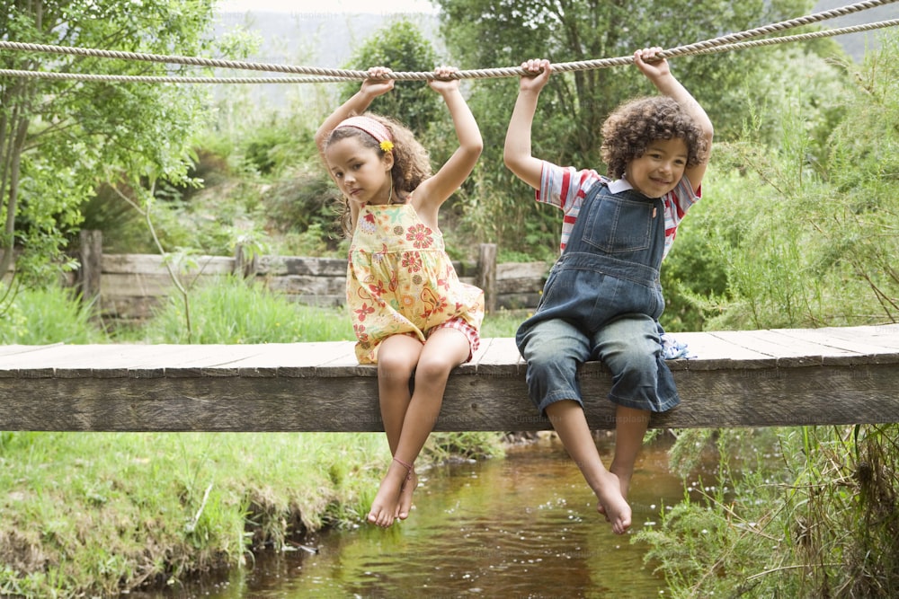 a couple of kids sitting on top of a wooden bridge