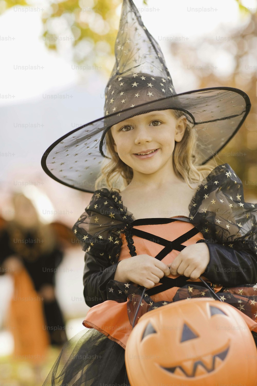 Una bambina in un costume da strega che tiene una zucca