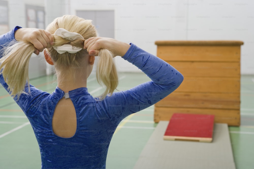 a woman in a blue shirt is putting her hair in a ponytail