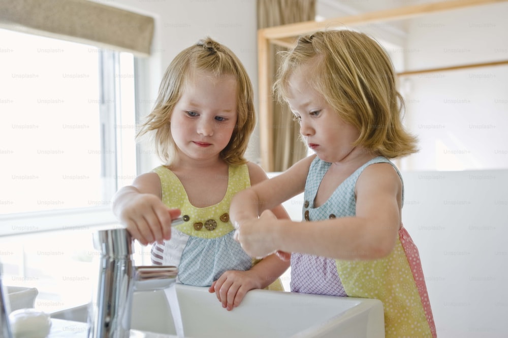 two little girls are washing their hands in the sink