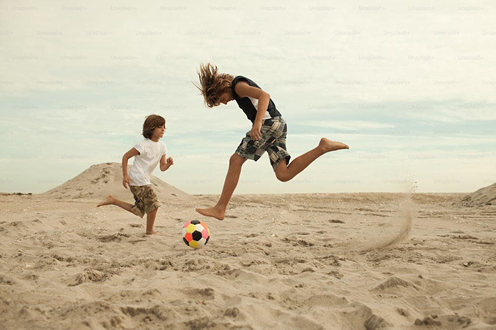 a boy and a girl playing soccer in the sand