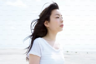 Una mujer parada en una playa con el pelo soplando en el viento