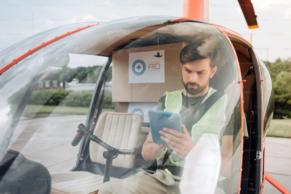 Final preparation. Handsome male volunteer seating in helicopter and looking at tablet