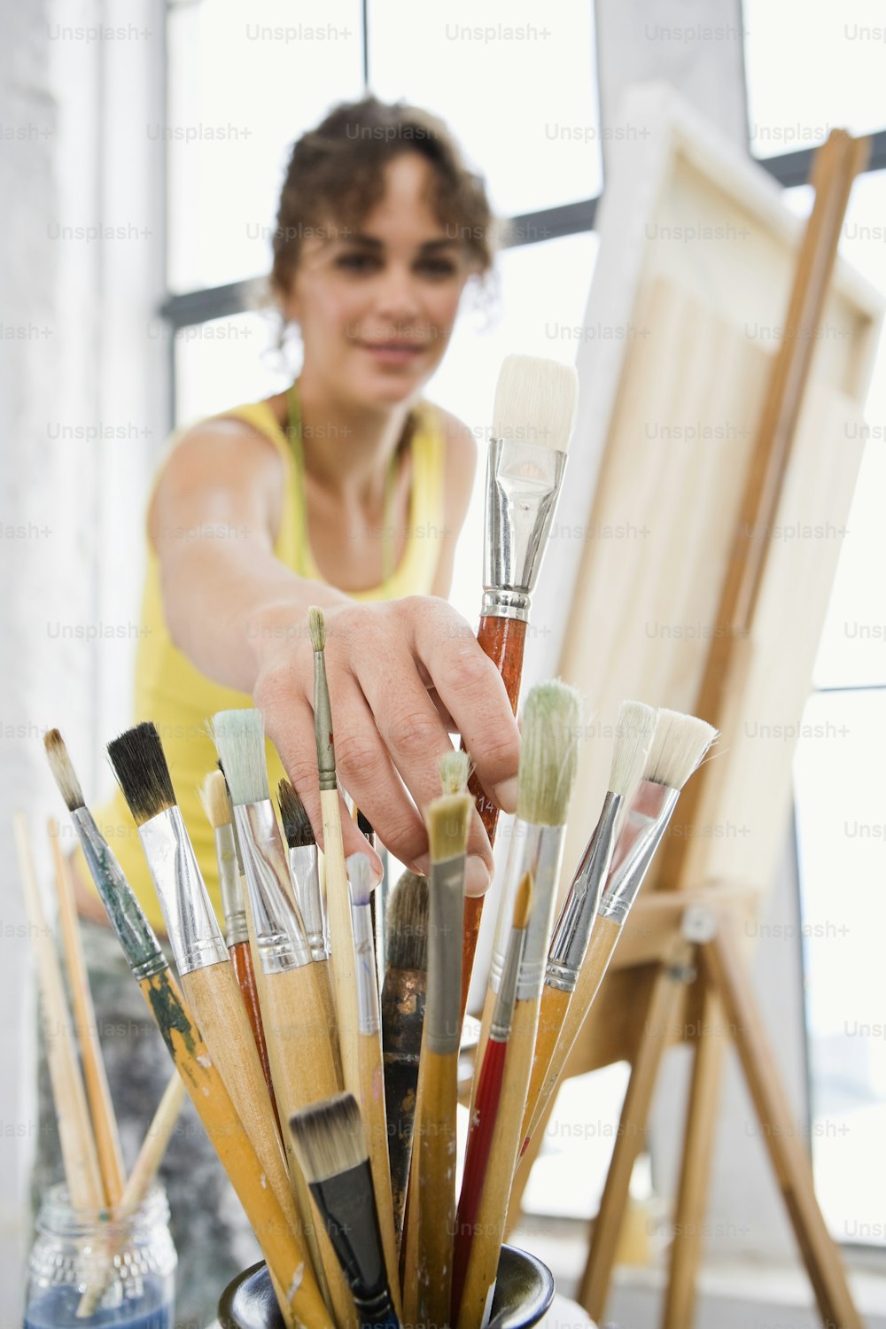 a woman is holding a paintbrush in a cup full of brushes