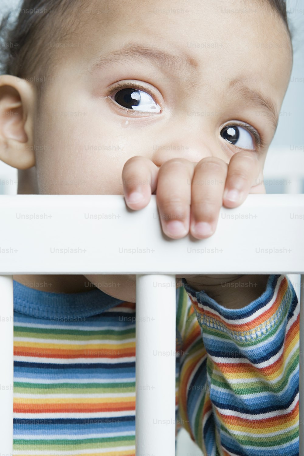 a baby peeking over the top of a white crib