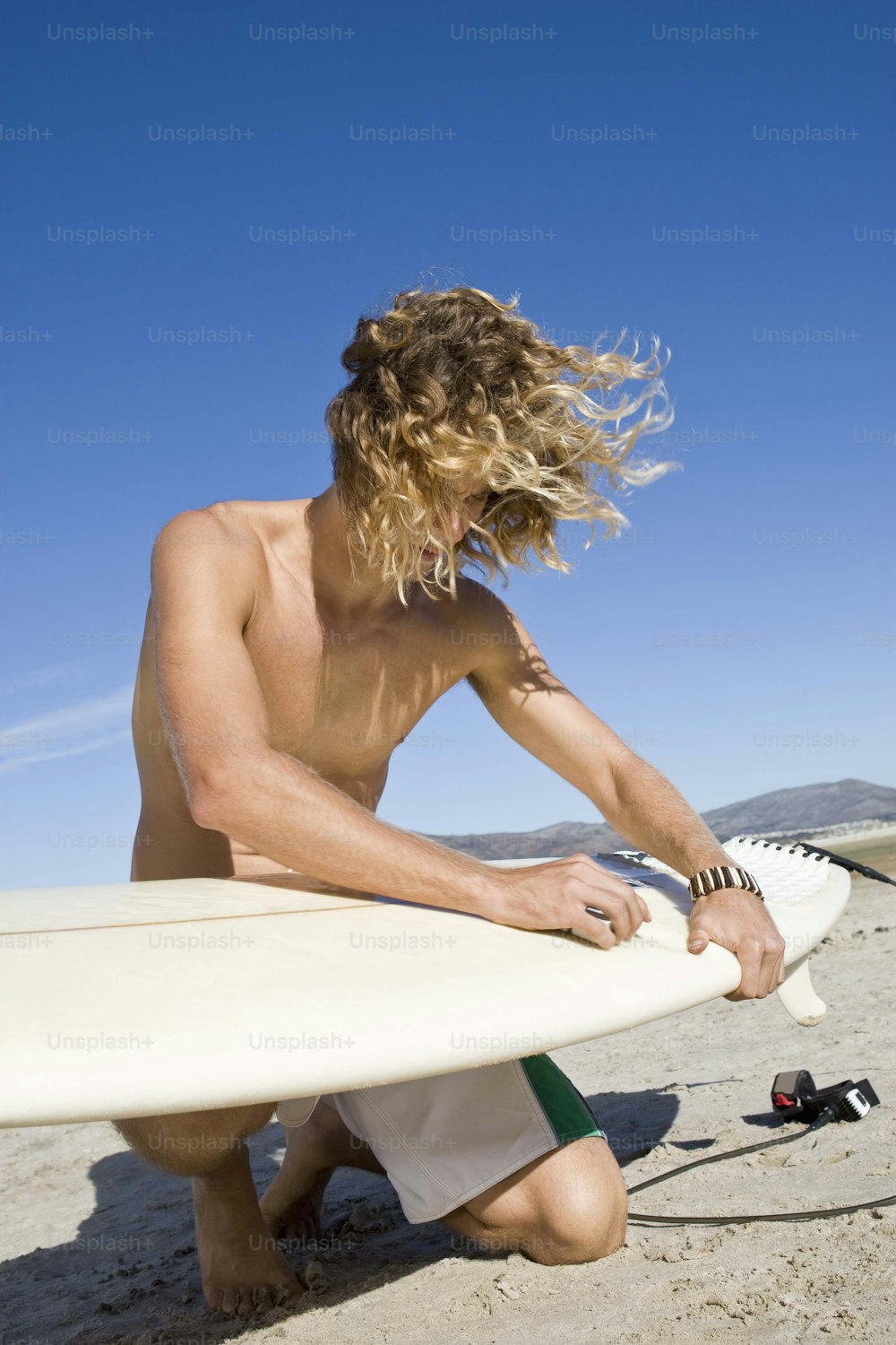 um homem sentado em uma praia segurando uma prancha de surfe