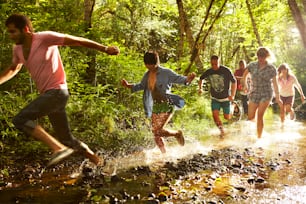 a group of people running through a stream in the woods