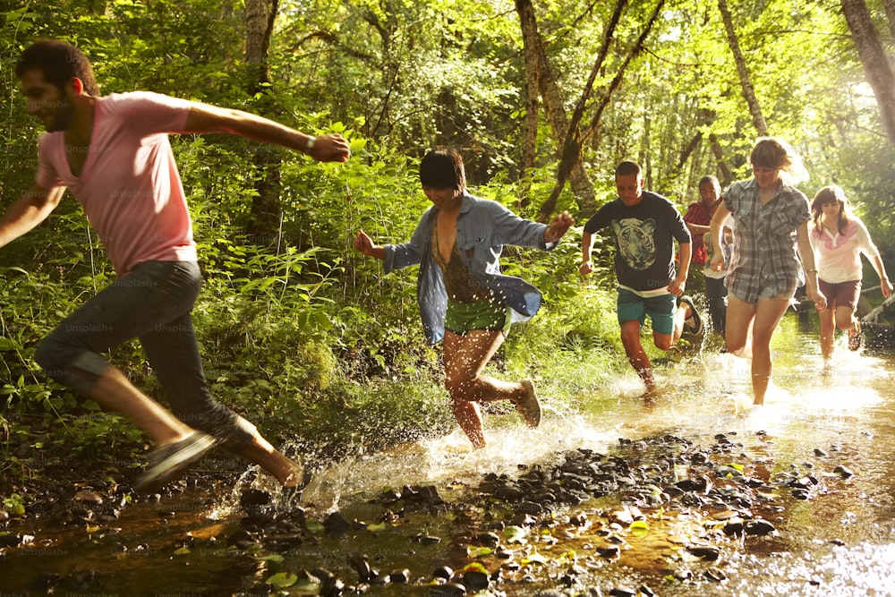 a group of people running through a stream in the woods