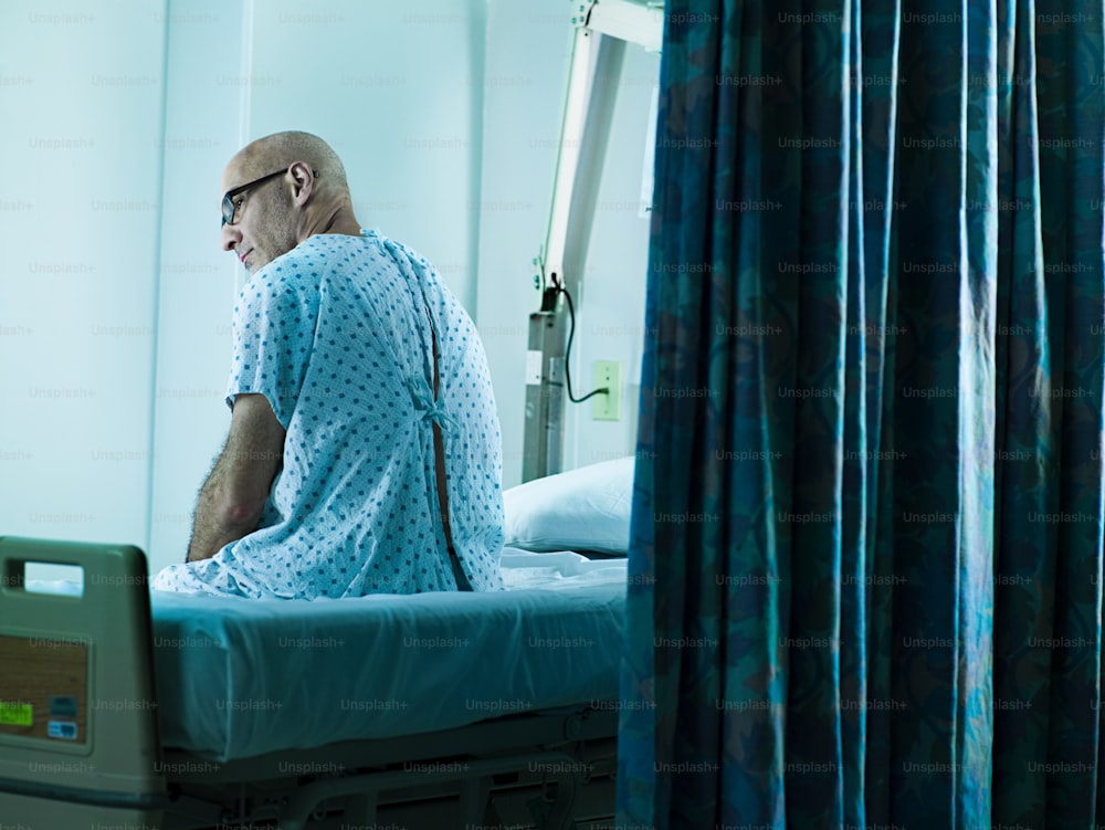 Ein Mann in einem Krankenhauskittel sitzt auf einem Krankenhausbett