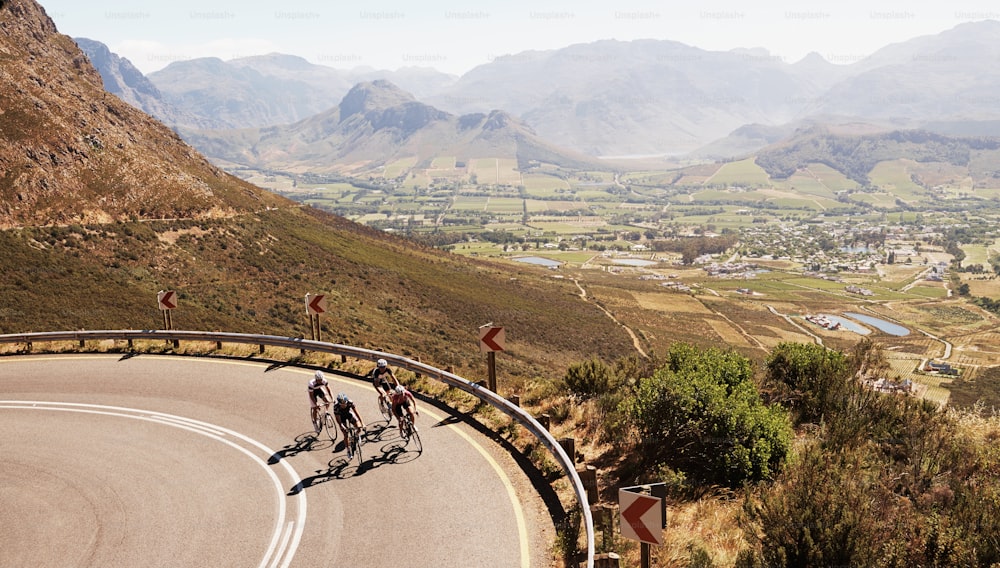 Long-distance shot of a group of cyclists riding on the road through a valley