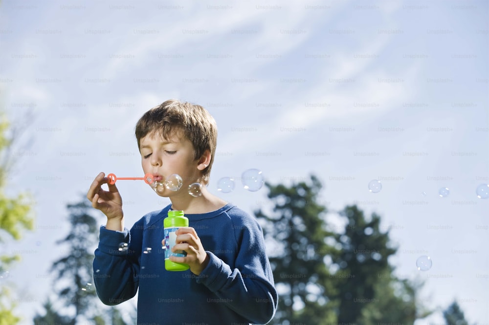 a young boy blowing bubbles with a green bottle