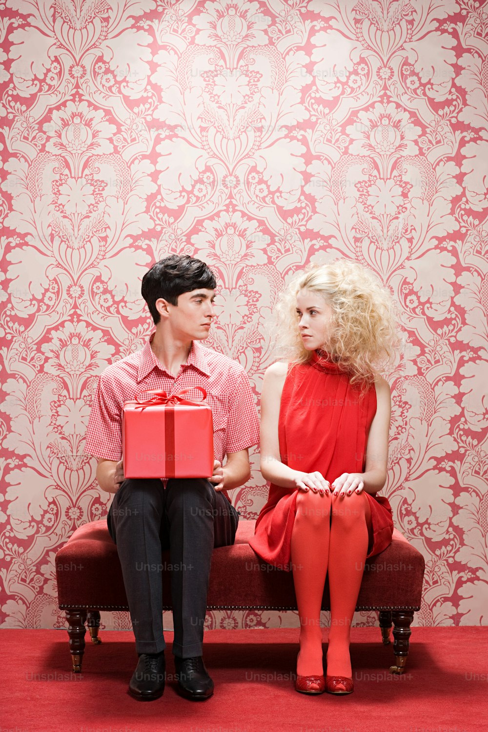 um homem sentado em um banco ao lado de uma mulher segurando uma caixa vermelha