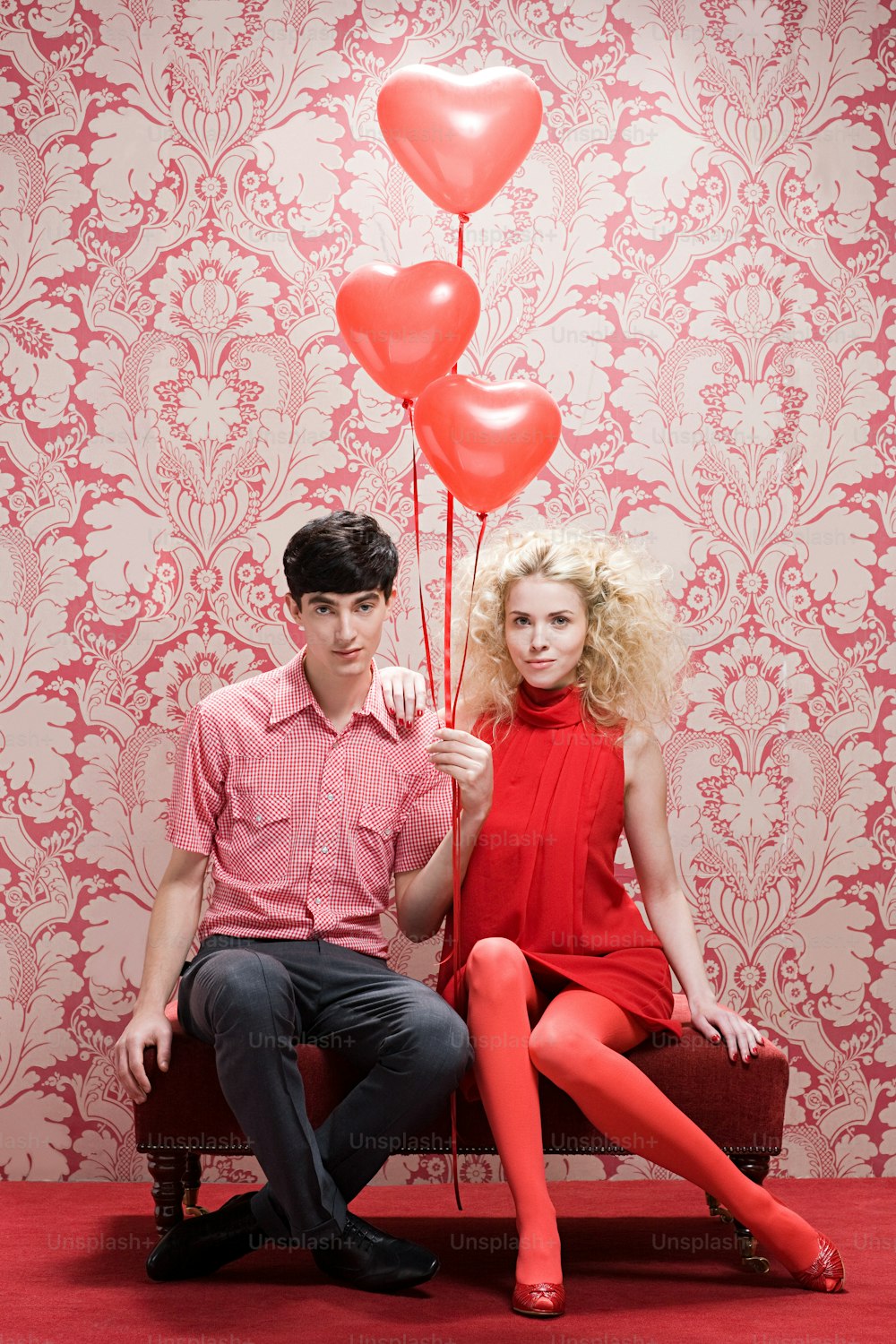 Un hombre y una mujer sentados en un banco con globos rojos