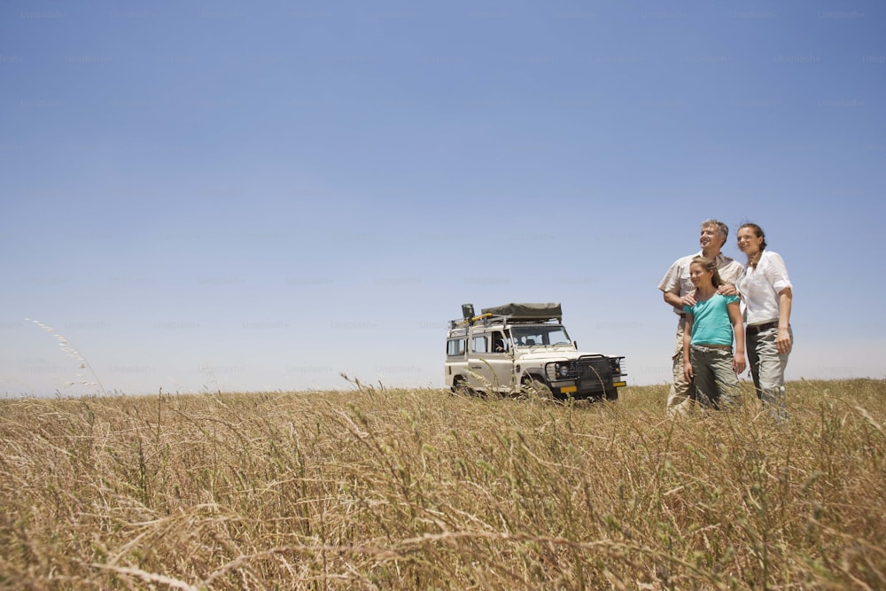a man and woman standing in a field next to a vehicle