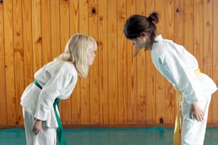 Dos chicas con uniformes de karate de pie frente a una pared de madera