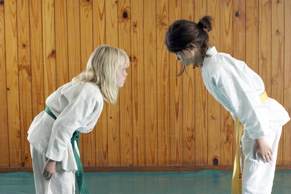 two girls in karate uniforms standing in front of a wooden wall