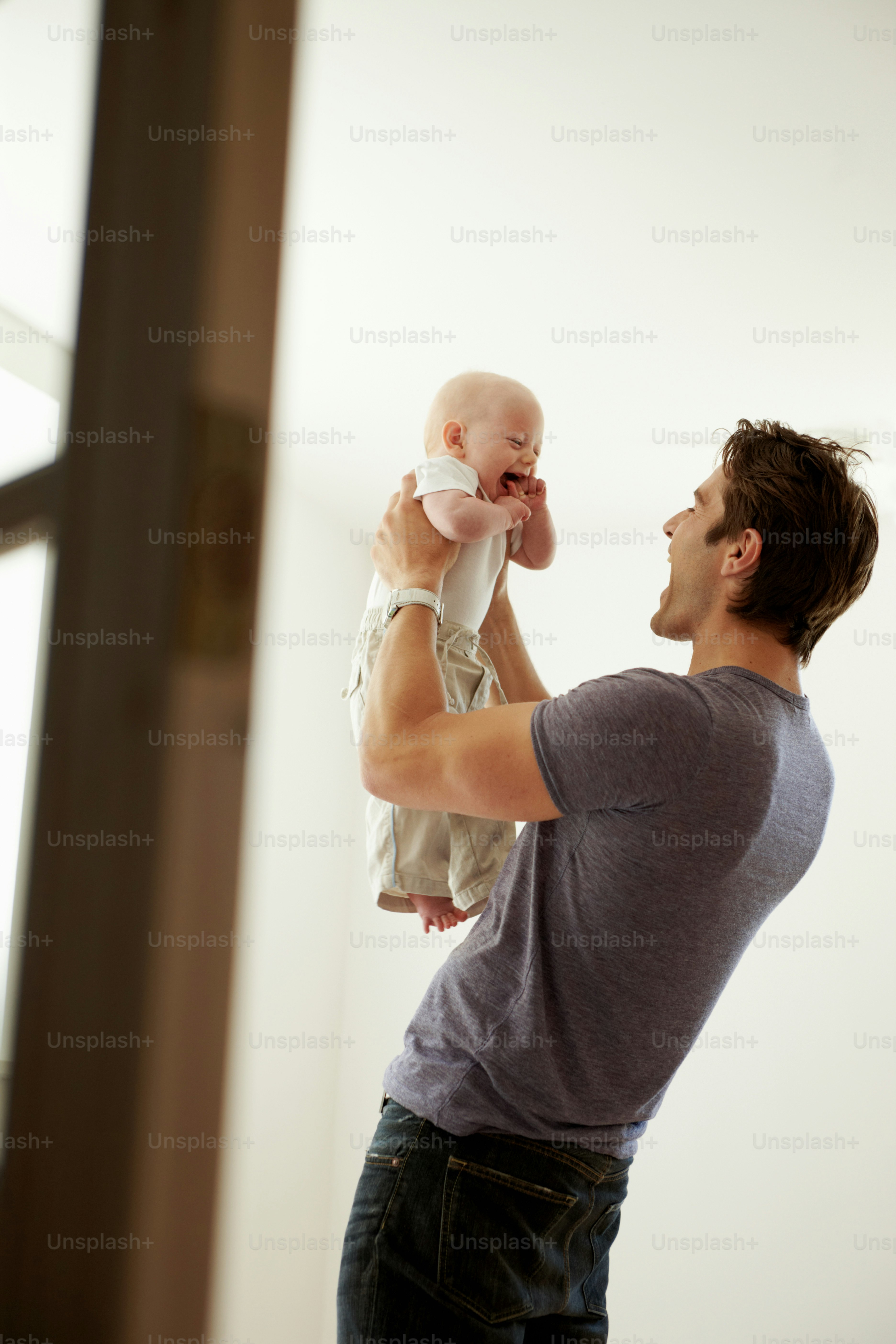 A candid shot of a father holding up his baby boy and gazing at him lovingly