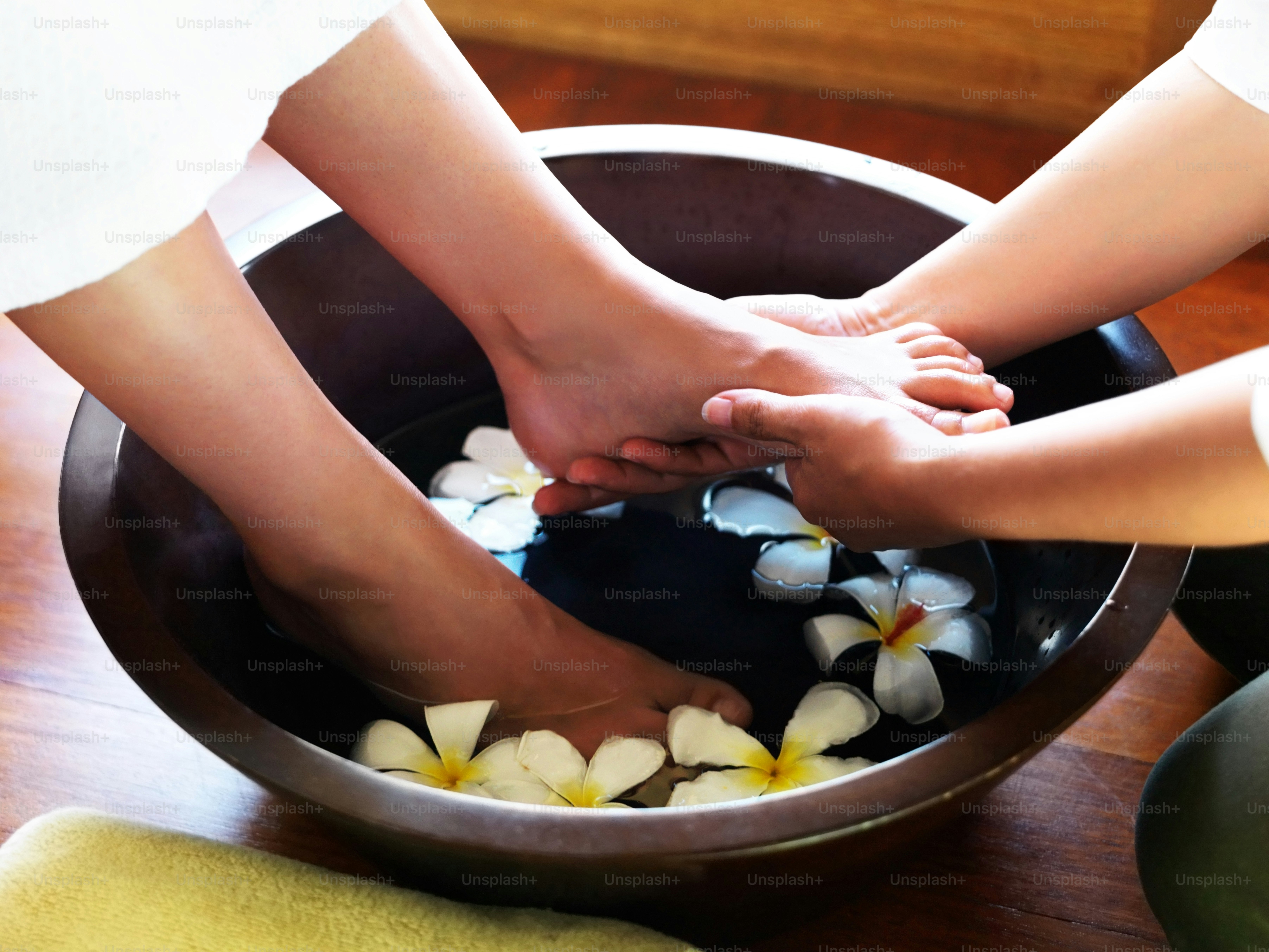 two people holding hands in a bowl of water with flowers
