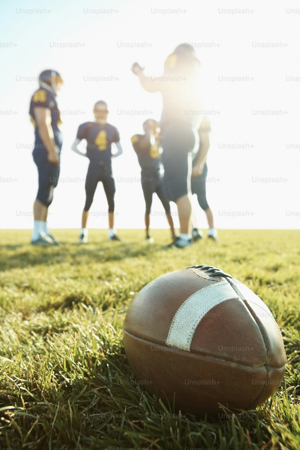 Close-up of an American football lying on a grass field with players in the background