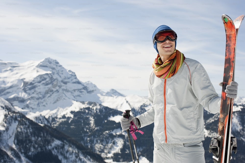 Un homme tenant une paire de skis au sommet d’une montagne enneigée
