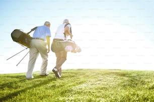 "A senior couple carrying their golf bags and walking along the fairway against a sunny, blue sky"